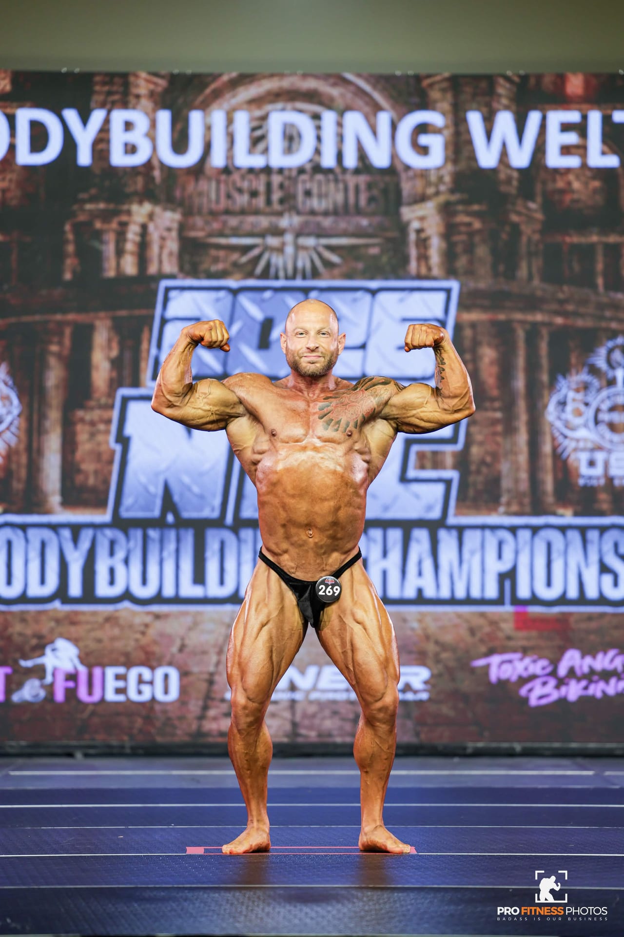 Eitan Bratin hitting a front double biceps on stage at an NPC bodybuilding championship